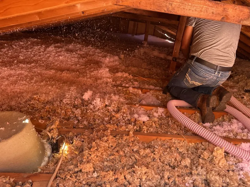 Crew member in an attic running the hose while blown-in insulation is installed