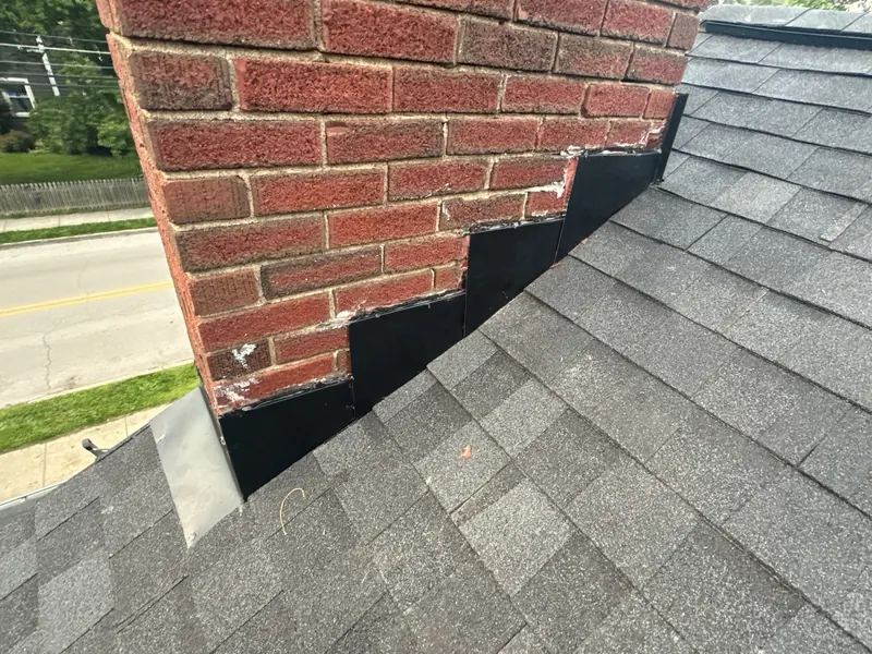 Fresh flashing sealed around a brick chimney on a dark shingle roof